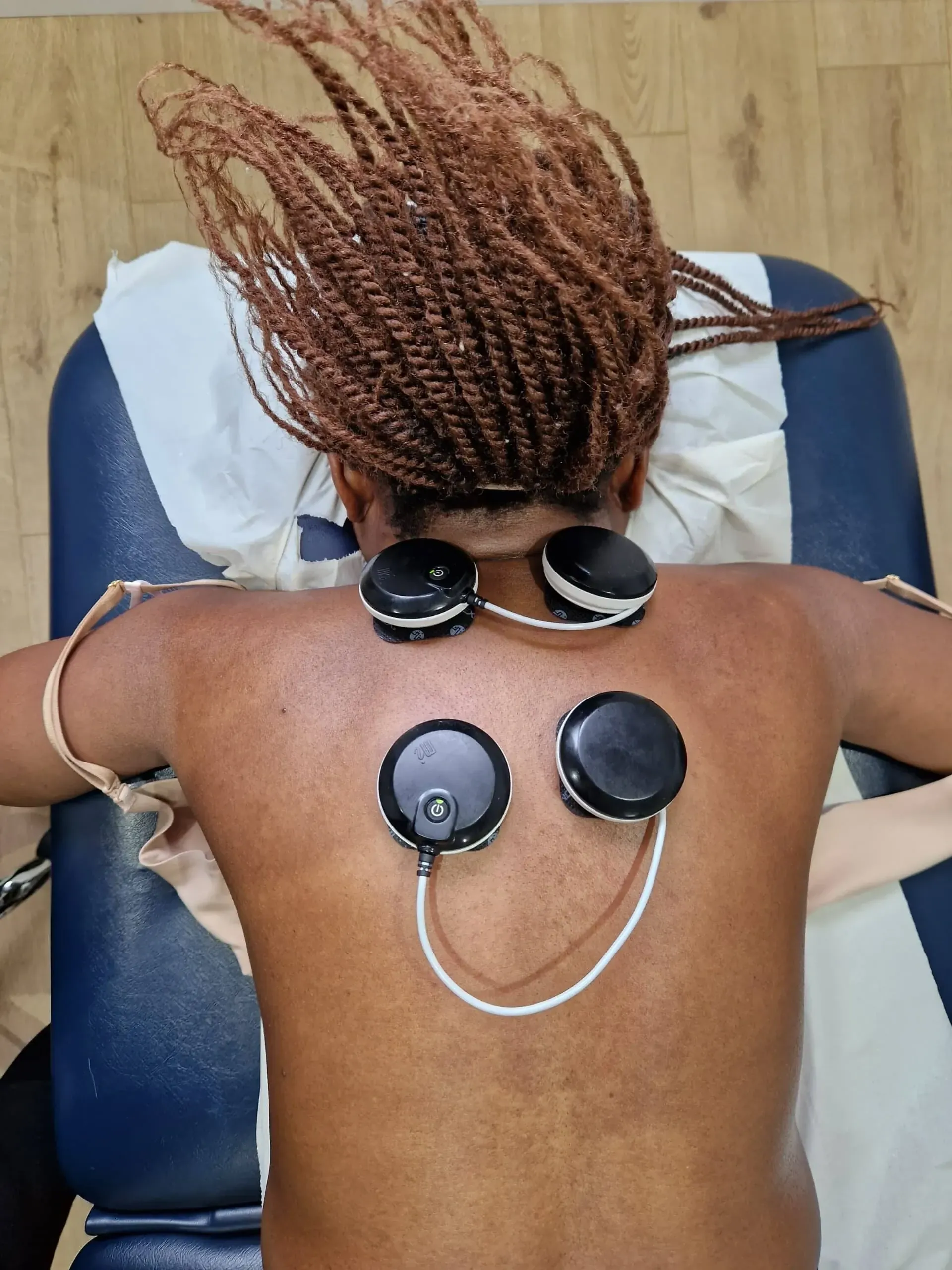 Physiotherapist applying electrical muscle stimulation (EMS) therapy equipment to patient's muscles for strengthening and pain management